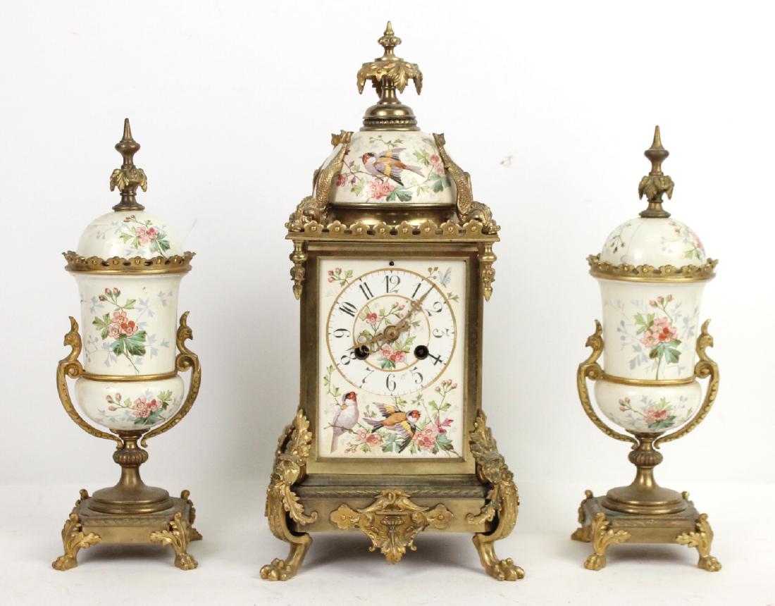 French Vincenti & Cie Three Piece Garniture: late 19th C. White and polychrome painted porcelain and brass. Comprising a clock and pair of lidded vases. The clock with dolphin mounted upper corners and the base with masked monopodia, the vases w