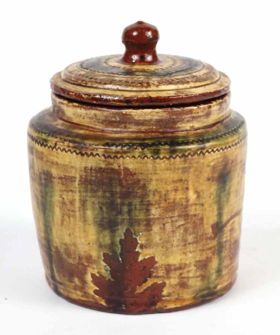 Slip and Stencil Decorated Redware Covered Jar: American, 19th C., Peace pipe, cannon, and gun decorated. 6"h x 5"dia. Provenance: Acquired at Sotheby's Deyerle Sale, May 1995.