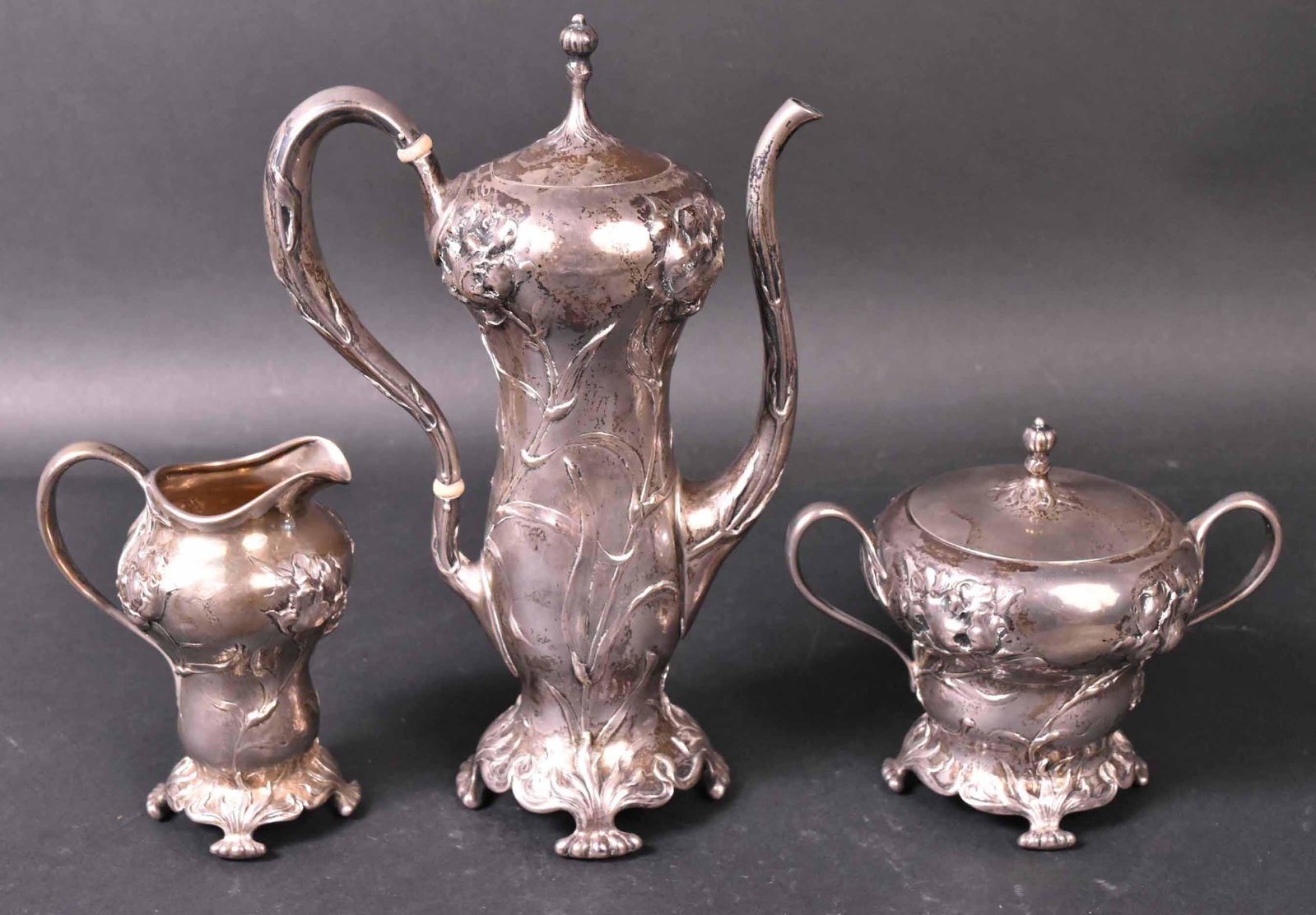 American Art Nouveau Sterling Coffee Set: Theodore B. Starr sterling silver three piece floral decorated coffee set. Comprising: a coffee pot, 10"h, covered sugar bowl and cream jug, total weight apx. 41 t.o. Provenance: Property from the Col