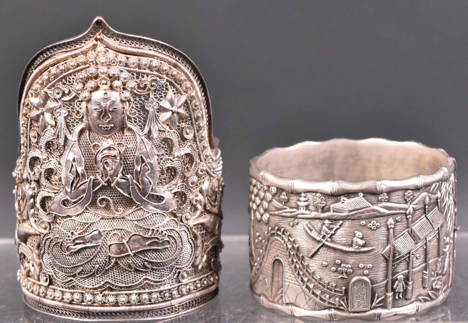 Chinese Silver Bamboo Decorated Cuff: Depicting scenes of village life. Unmarked. Together with a Chinese silver filigree Buddha decorated cuff. Stamped, "Silver China". 3.5"h Provenance: Property from the Collection of Myrna and Bernard 