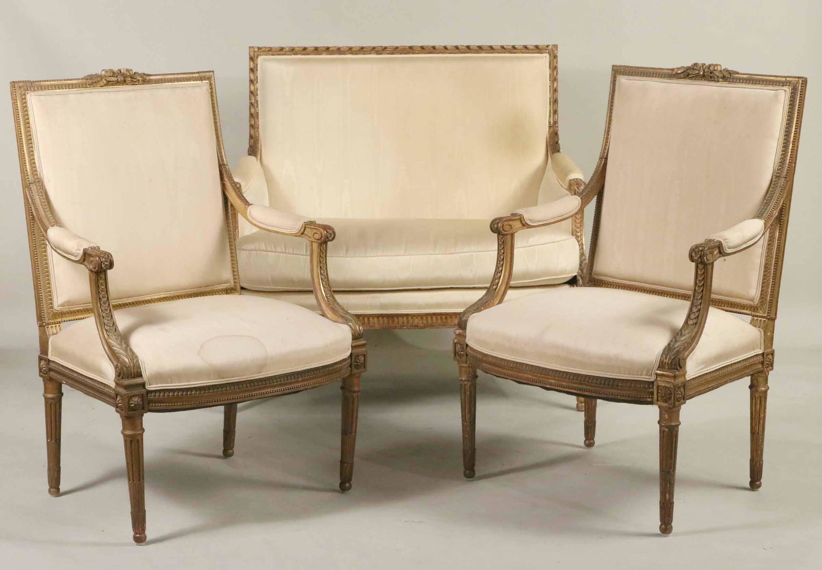 Louis XVI Style Suite of Seating Furniture: Comprising, a canape and a pair of fauteuil. Wear to giltwood, stains to fabric, and losses. 39-1/2"h x 26"w x 21"d and 39-1/4"h x 43-1/2"w x 23"d