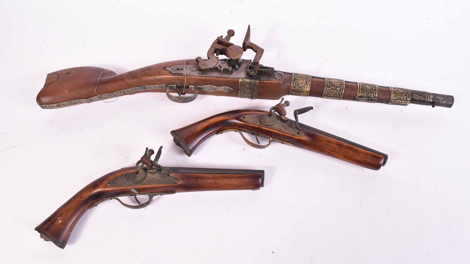 Three Decorative Flintlocks: 19th C., non-operational, including a pair of pistols and one in the style of a Middle Eastern short stocked musket. 13"l and 26-1/2"l
