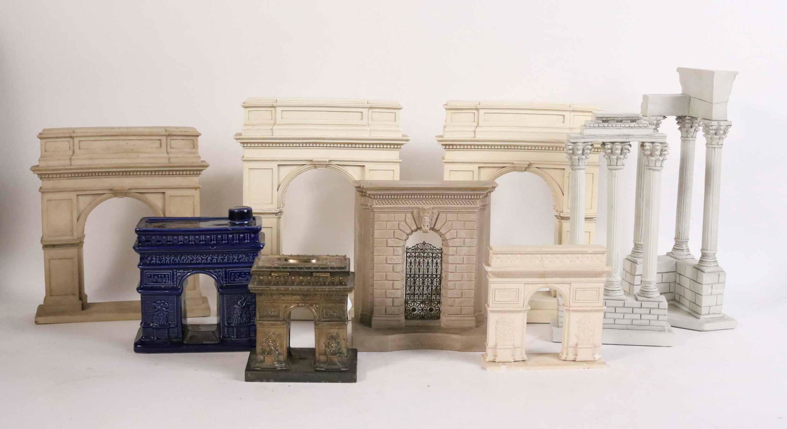 Group of Nine Architectural Models: Comprising, a ceramic decanter of the Arc de Triomphe, a patinated metal Arc de Triomphe, a porcelain Arc de Triomphe, two composition Temple of Vespasian Columns, The Burlington House Arch, and three