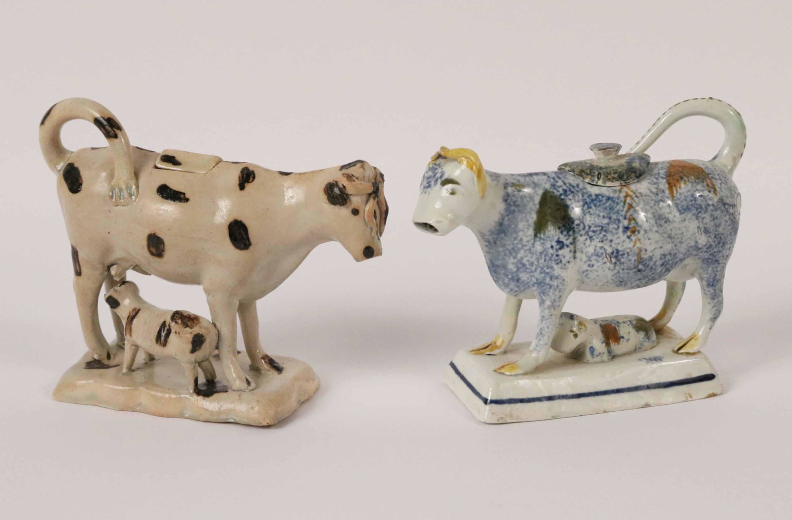 English Staffordshire Pearlware Cow Creamer: 18th C. Depicting a cow standing above a recumbent calf, decorated with blue, green, yellow and brown sponge decoration, on a rectangular plinth; the upturned tail forms the handle, with fitted lid on
