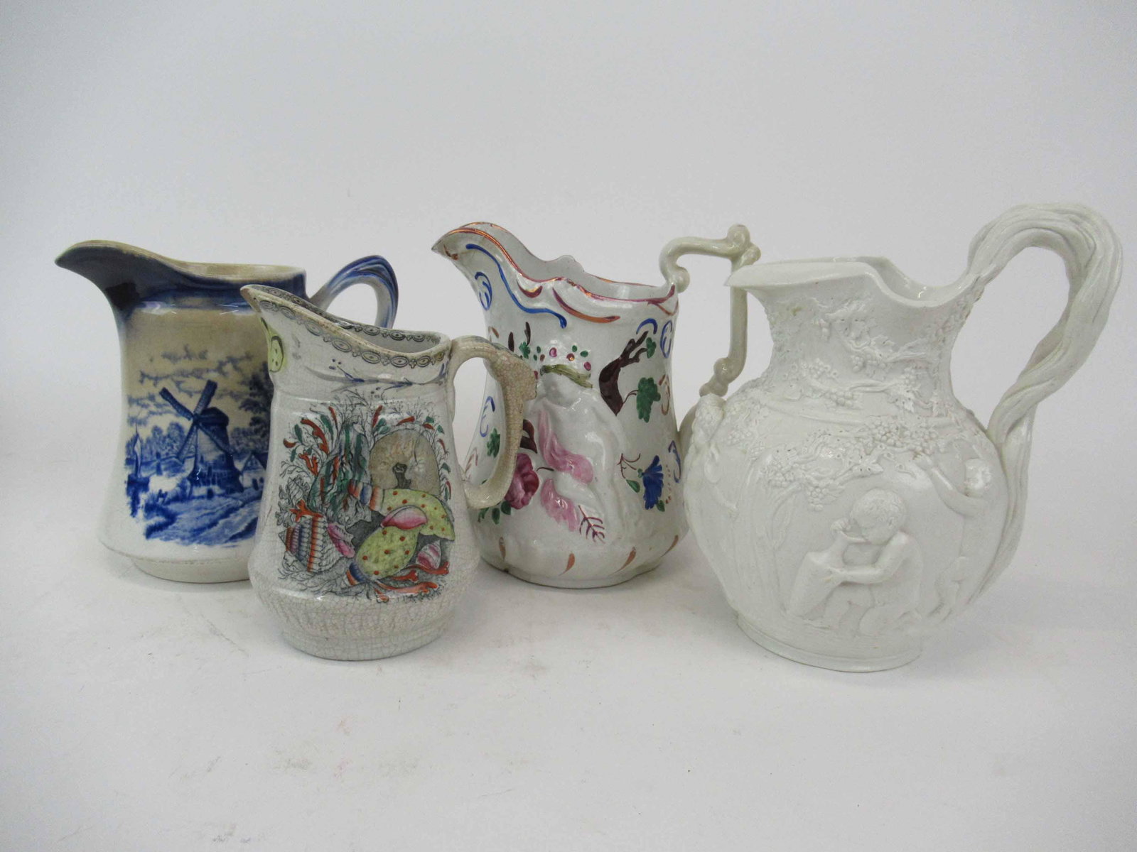 Antique Copeland and Garrett Parian Jug: Antique Copeland and Garrett Parian Jug. Together with three assorted jugS with Putti decoration and windmill decoration. Used Condition, wear, worn, chips, repairs, crazing. Parian vase has chips to 