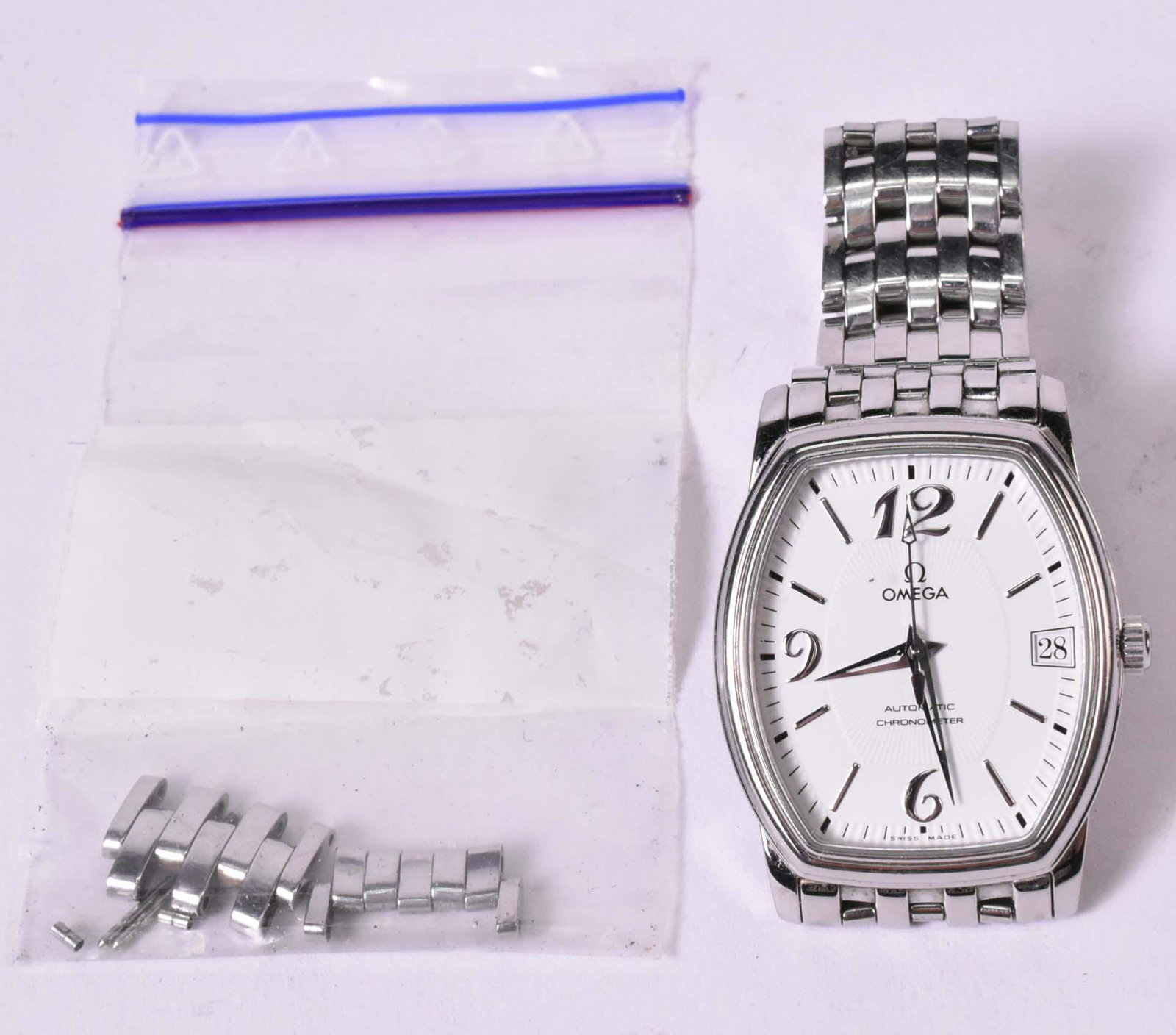 Omega Automatic Chronometer Mid Size Wristwatch: Tonneau shape white enamel dial with silver tone Arabic Numerals at 12,6,9, other stick numeral indicators, date window at "3", 30mm wide x 33mm long, on bracelet band with Omega symbol on clasp.