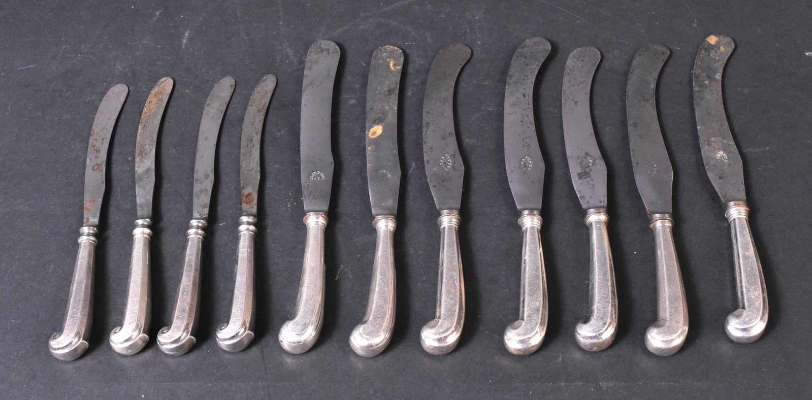 Eleven English Silver Pistol Handled Knives: 18th Century. Comprising set of five, with large scimitar carbon steel blades stamped "London Made", two with less pronounced blades, crested with engraved griffins on coronets, each 9-1/4"l, four sma