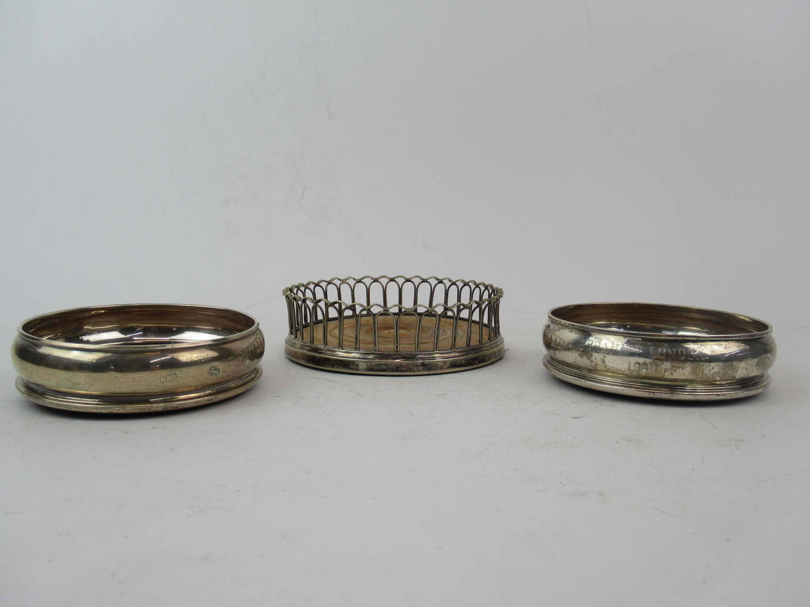 Pair of English Silver Wine Coasters Caddys: Pair of English Silver Wine Coasters Caddys. Each Inscribed Braniff London 1980 and hallmarked M & H. Together with a open work style bottle coaster caddy. Used condition, wear, worn. Pair of coasters