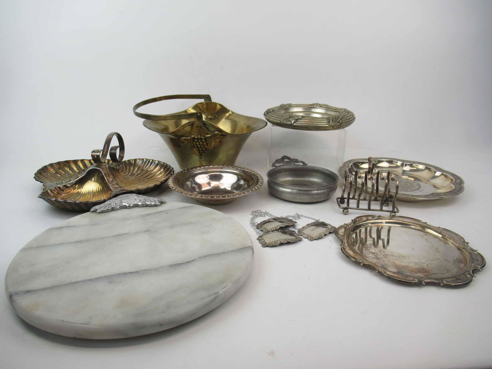 Group of Assorted Silver Plated Table Articles: Group of Assorted Silver Plated Table Articles. Including, brass grape basket, liquor tags, shell form condiment dish, Gorham Chinese, bowl, toast holder, metal caddys, marble cheese block and pewter