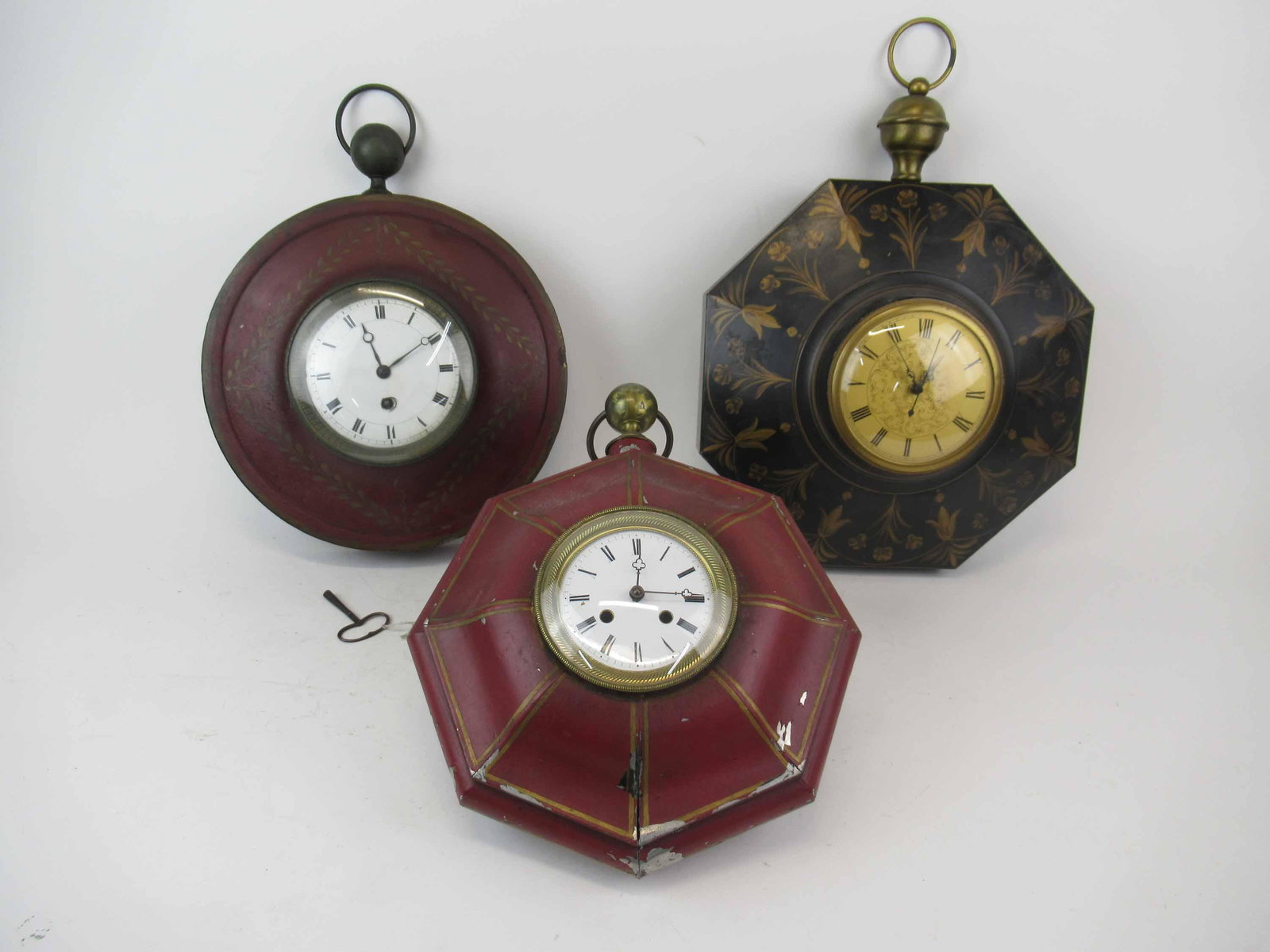 Two Toleware Red Painted Wall Clocks: Two Toleware Red Painted Wall Clocks each with gilt decoration and enamel clock face. Together with a similar black toleware clock with gilt decoration. Used condition, wear, worn, paint loss, dents m