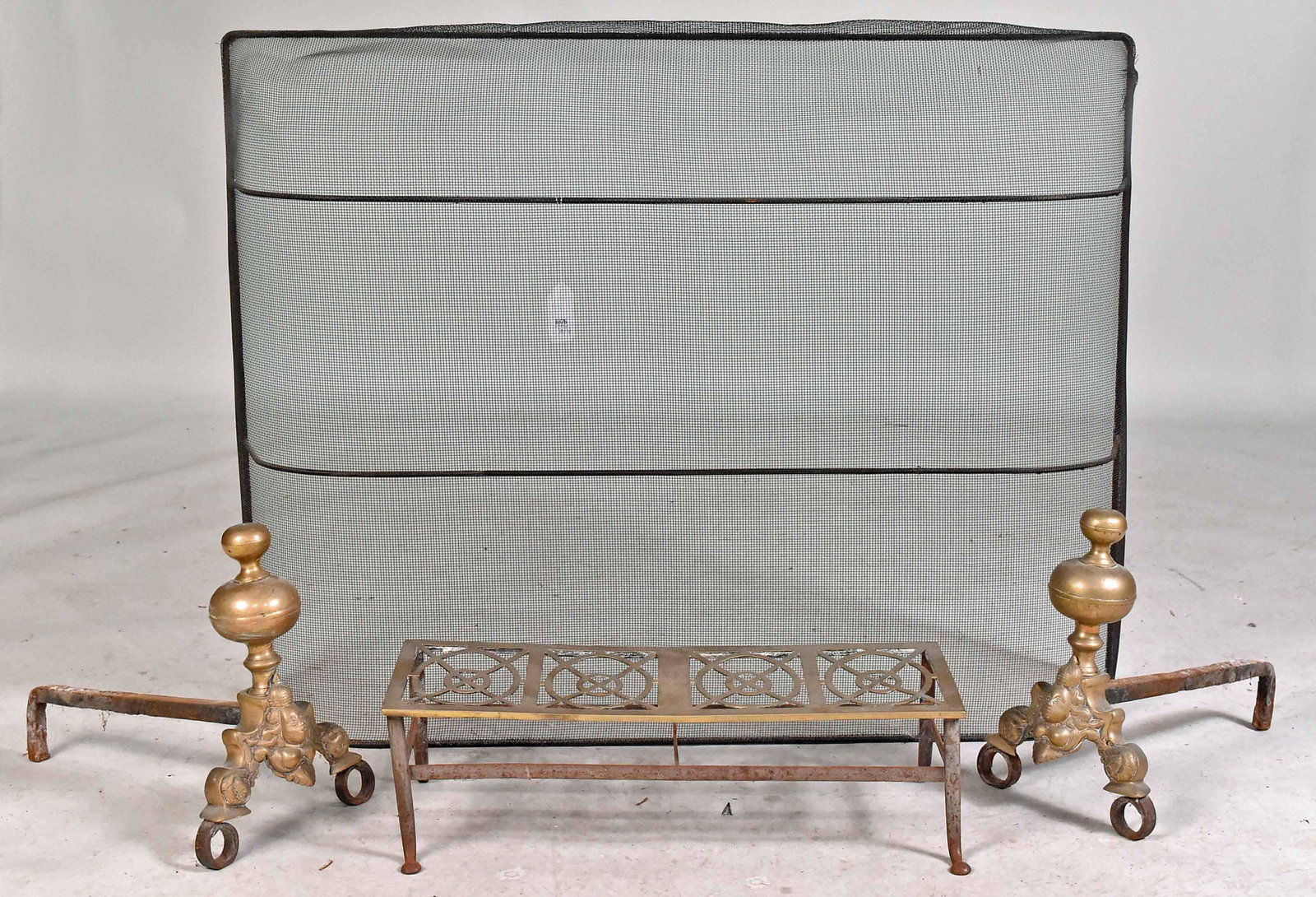 Pair of George II Style Bronze Andirons: Early 20th C., each with mask decoration, 14"h. Together with a brass and wrought-iron footman, with four pierced oval reserved, 24"l and a black-painted wirework spark screen, 33"h x 44"w. 4 pieces P