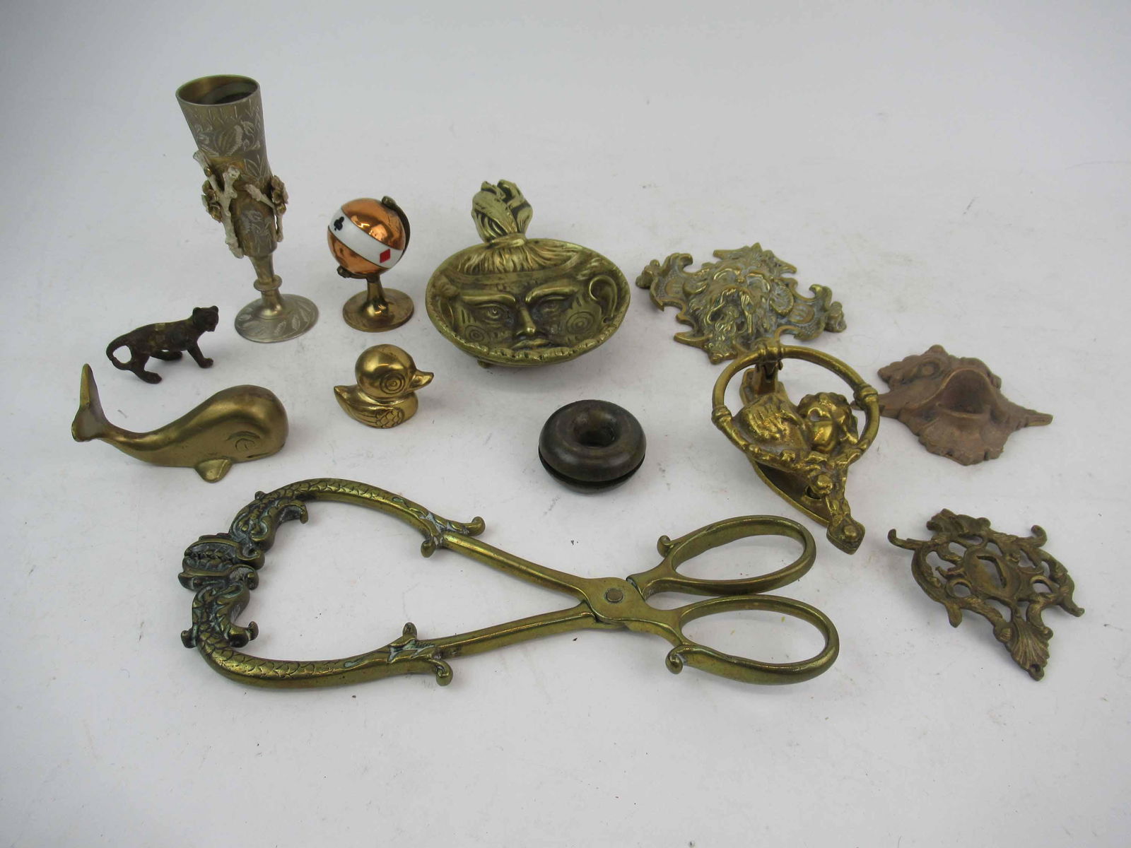 Group of Assorted Brass Table Articles: Group of Assorted Brass Table Articles. Including tongs, kissing door knocker, whale, duck, escutcian, vase, lion, figural wall mount, figural dish and a card suite globe. Used condition, wear, worn.