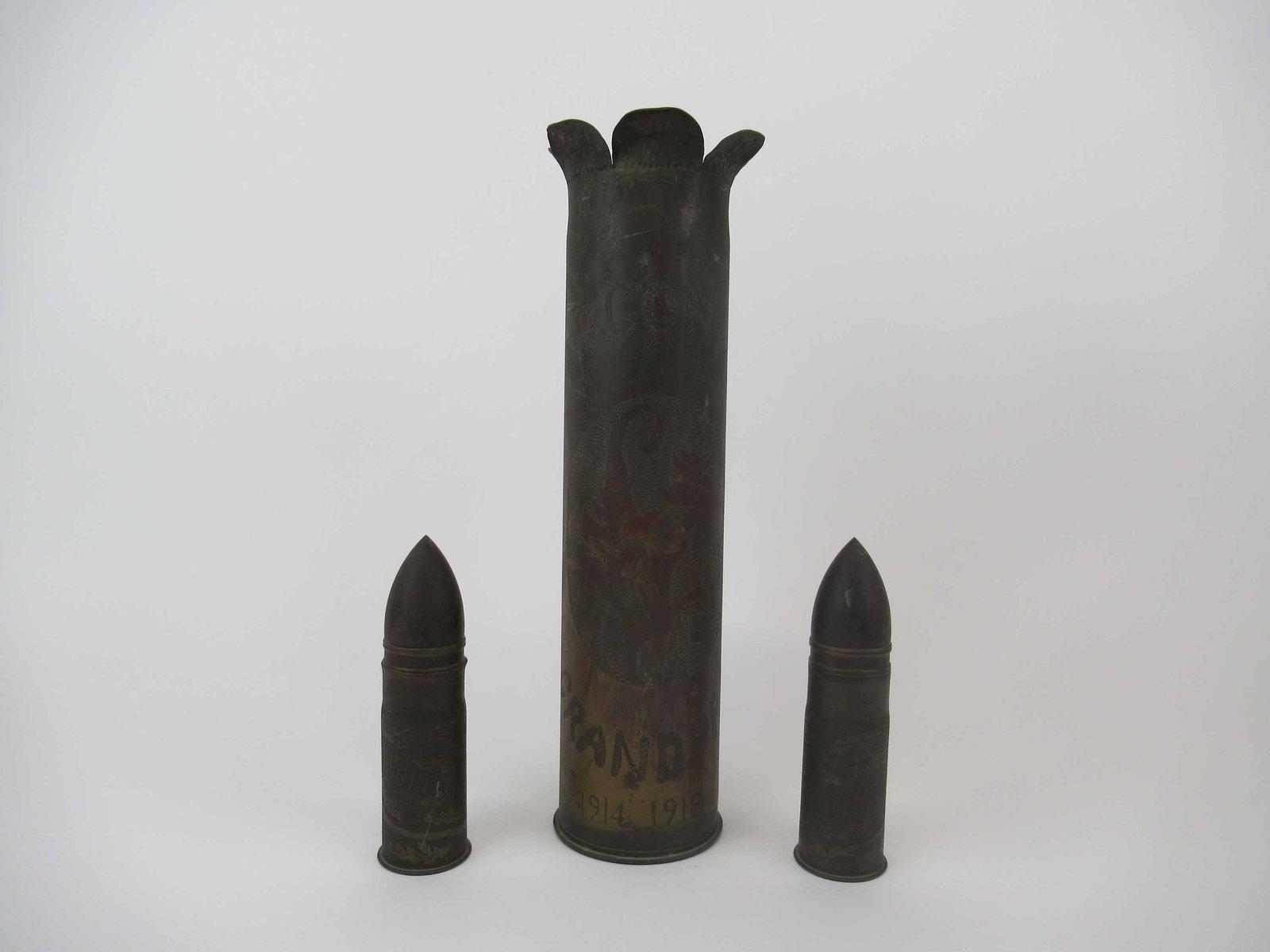 WW I Argonne Grandpre Trench Art Shell 1914-1918: WW I Argonne Grandpre French Trench Art 75mm Shell 1914-1918 with daffodil motif. Together with two smaller shell. Used condition, surface oxidation. 13 1/2" tall x 3 3/8" diameter