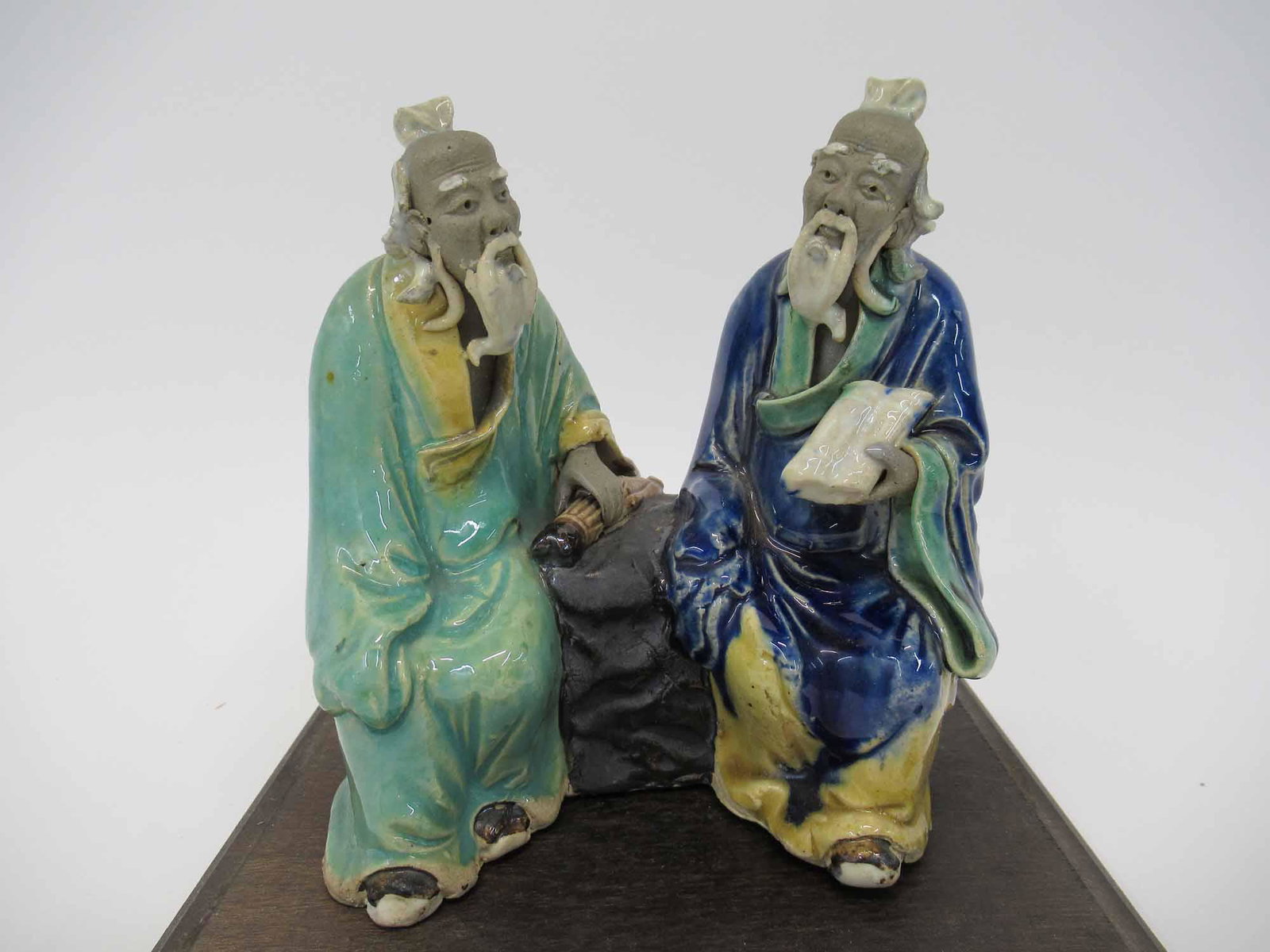 Oriental Earthenware Figural Group: Oriental Earthenware Figural Group depicting 2 seated elders, together with Lucite display case on wooden base. Used condition. Figures Stand 5 1/4" tall x 5" x 3"