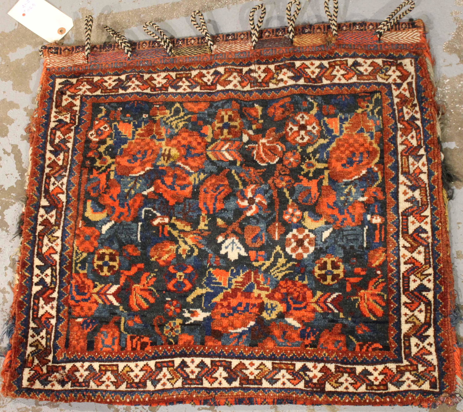 South Persian Storage Bag: C. 1900, the cobalt field with European-style flowers overall within a narrow ivory meander border, with a kilim backing and loops. 28"l x 25"w Slevage is slightly tattered.