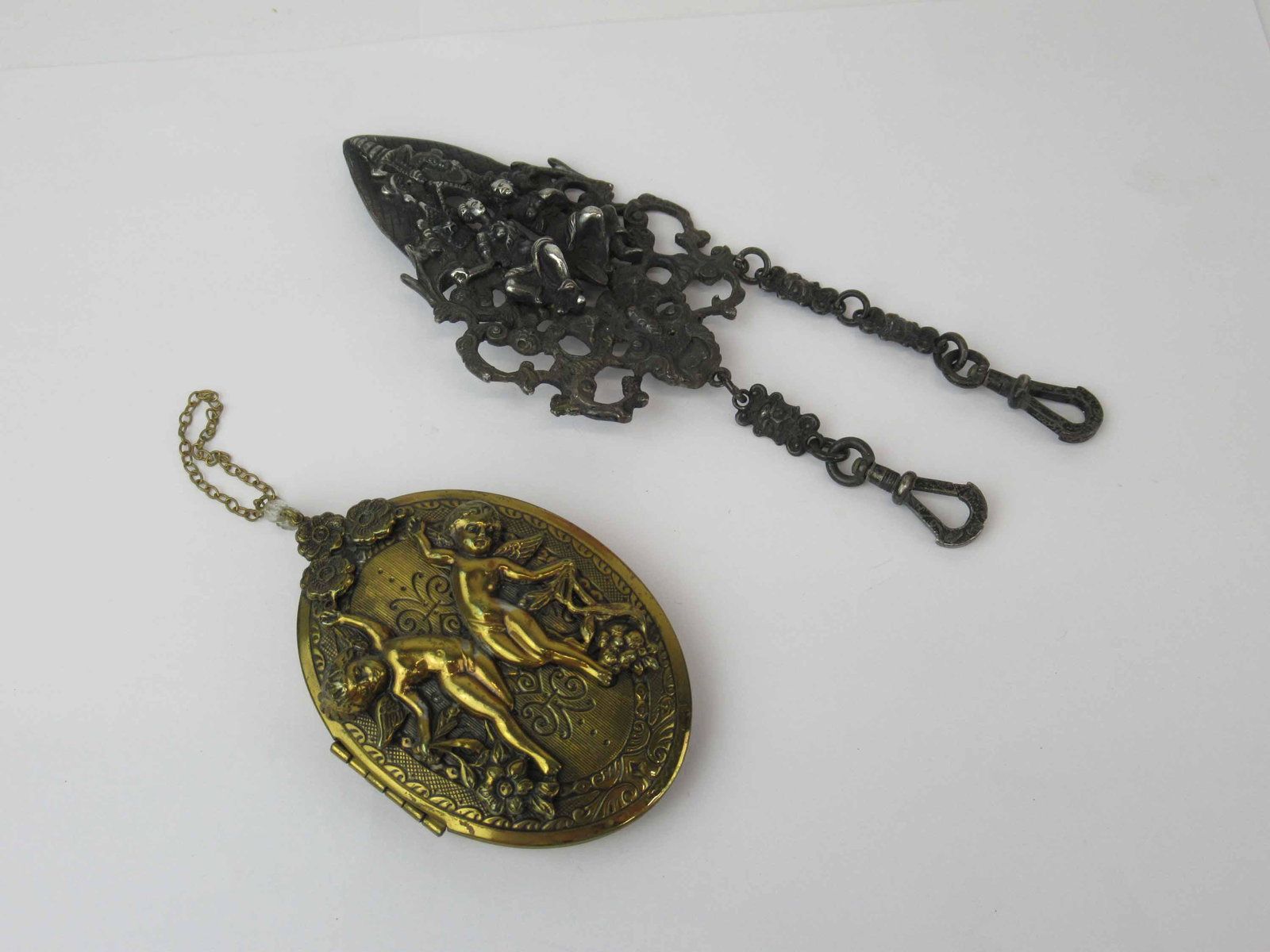 Antique Victorian Silvered Chateliane: Antique Victorian Silvered Chateliane depicting courting couple. Together with a Victorian Style gold tone locket with cherub. Used condition, Chateliane missing pieces and measures 5 1/2" x 2" wide.