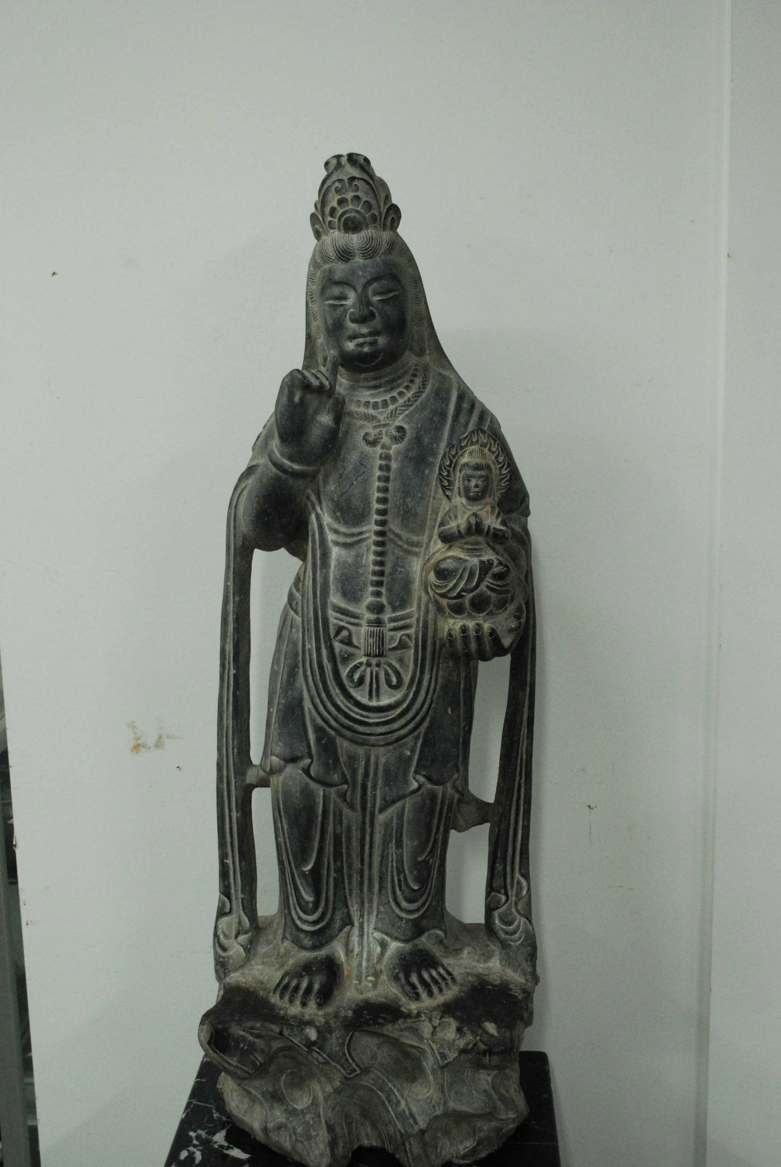 Kwan Yin Deity Carved Stone Statue With Buddha: Kwan Yin Deity Holding Buddha Carved Stone Statue. Together with a black granite base. Used condition. Statue is about 190 lbs, measures 39 1/2" tall x 13" wide x 10" deep and base 24" tall x 12" x 16