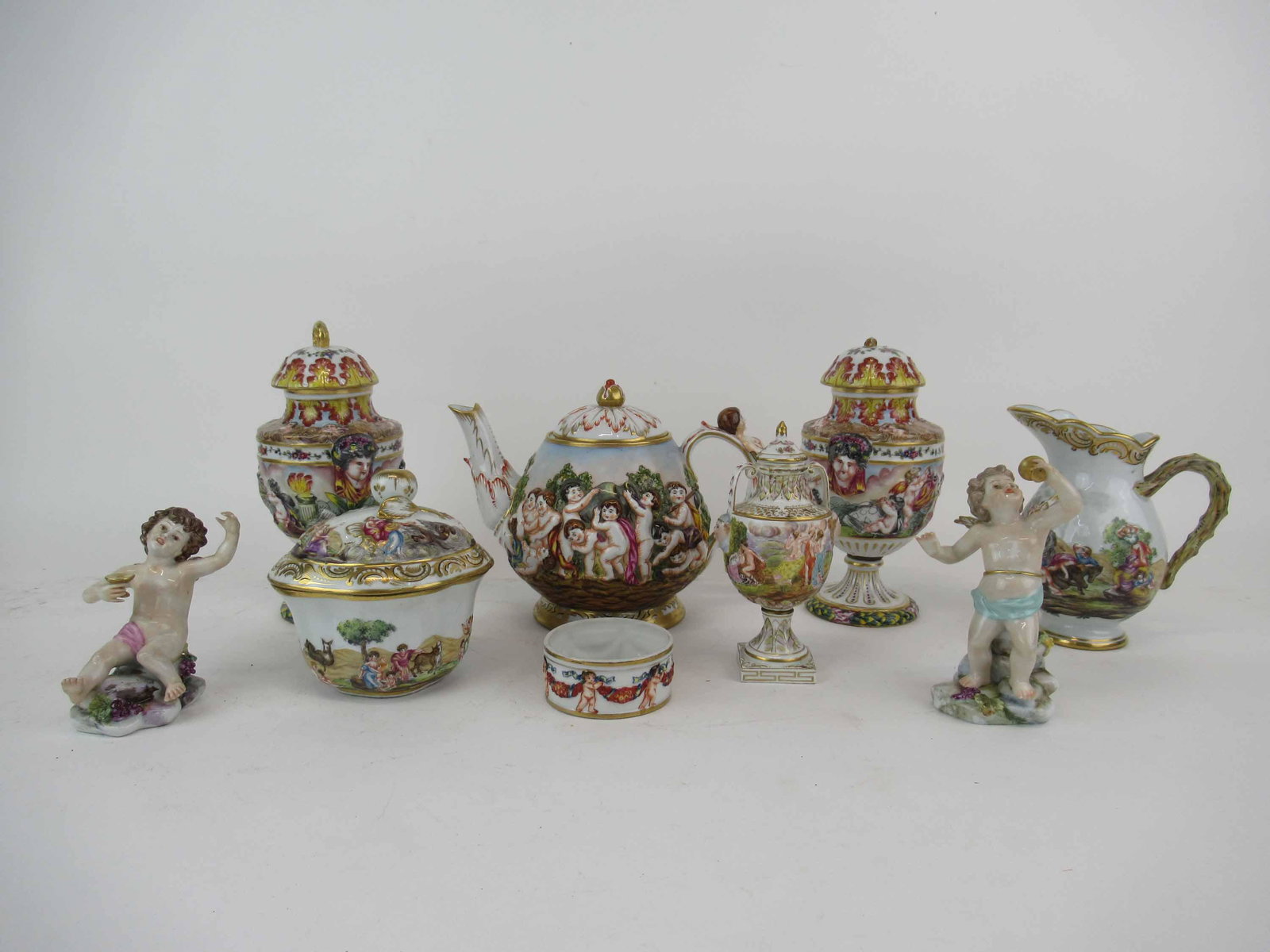 9 Assorted Capo Di Monte Table Articles: 9 Assorted Capo Di Monte Table Articles. Including tea pot, creamer, sugar, pair of urns one with broken handle, one small urn, 2 figures one with broken finger and small dish. Largest urn measures 7 