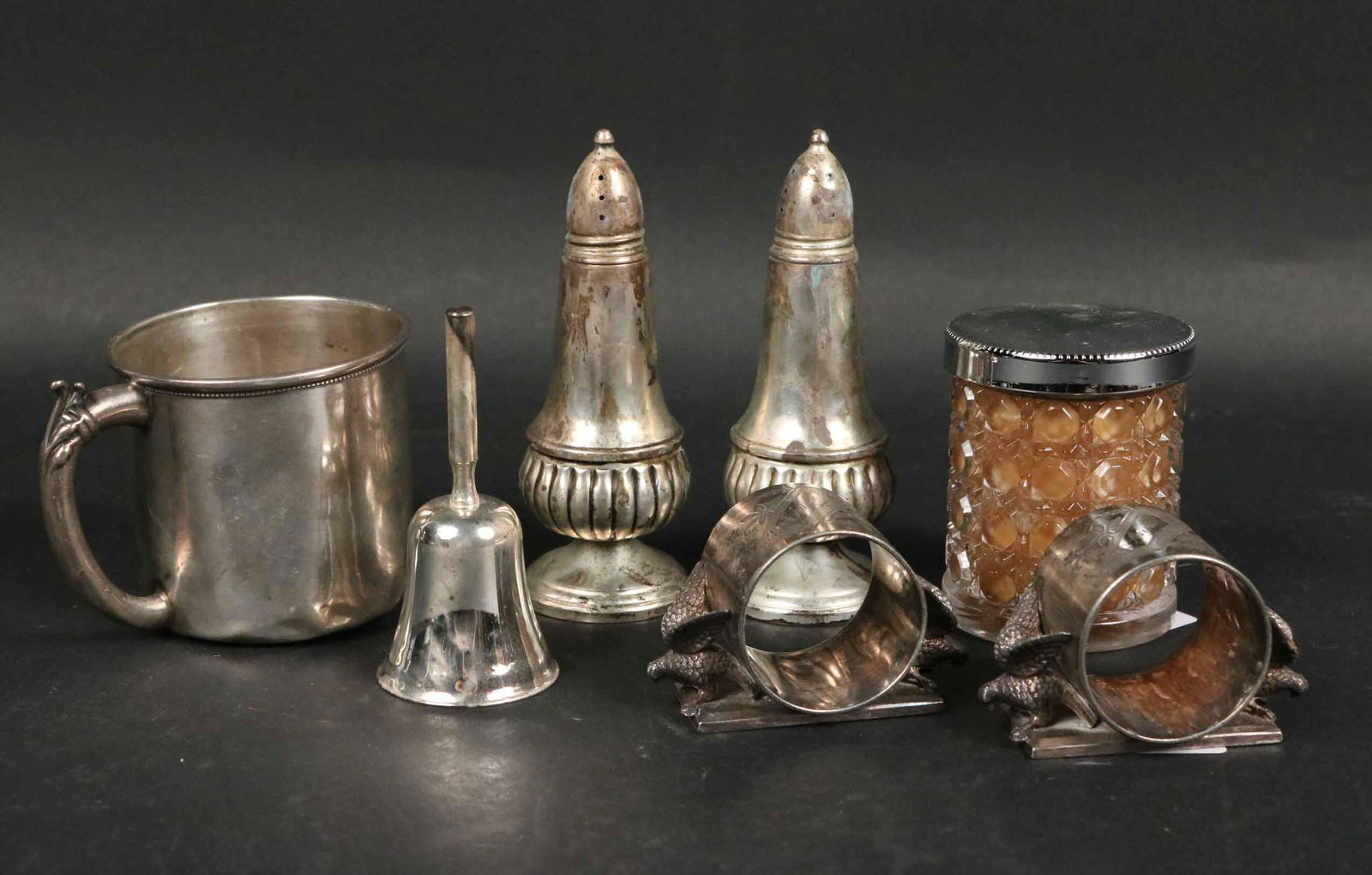 Vintage Sterling Silver Handled Cup: Together with a pair of Crown weighted sterling caster style salt and pepper, a pair of Meriden silver plated eagle decorated napkin rings, a metal bell, and a decorative candle. Dings and distressed.