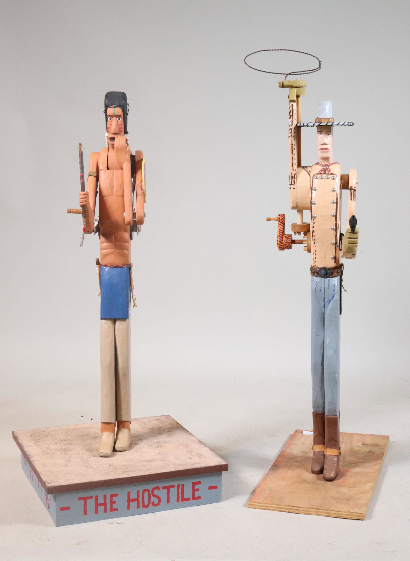 Two Carved & Painted Articulated Folk Sculptures: One signed John D. Young, dated 1992. Titled "The Hostile" depicting a cowboy and Indian. Cowboy: 46"h x 11-1/2"w x 24"d Indian: 41"h x 18-1/4"w x 18"dProvenance: Property from the Steve and Stephanie