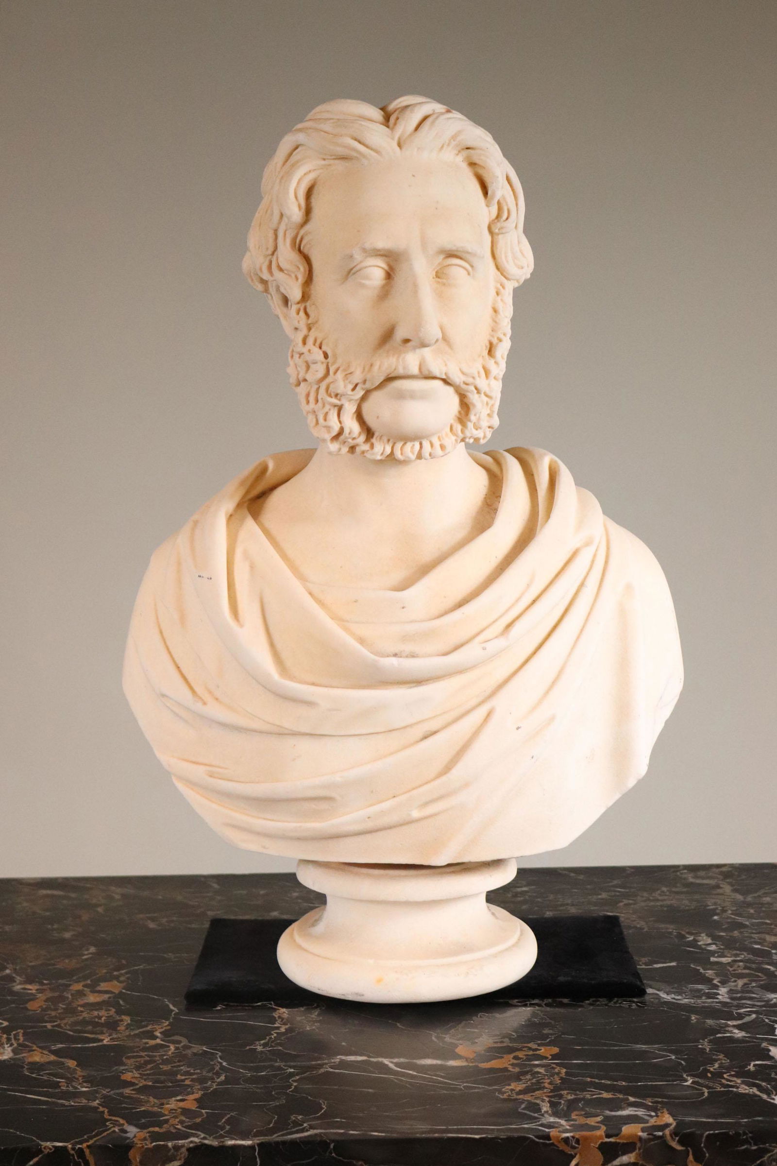 Classical Style Carved Marble Bust of Bearded Man: Possibly American, 19th/20th C. Large chip to base of socle. 28"h x 23"w x 11"d Provenance: Property from the Estate of William Hodgins, Boston, Massachusetts