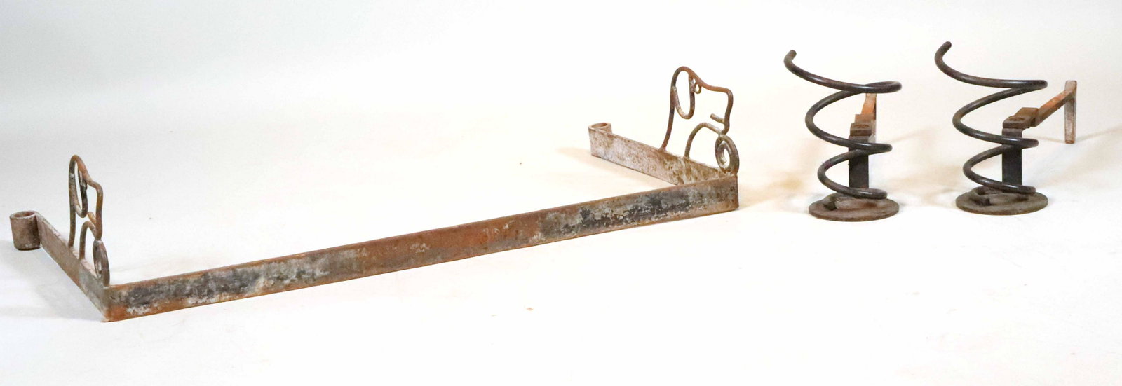 Pair of Wrought-Iron Spring-Form Andirons: Together with a wrought-iron dog-form fender. 3 pieces Andirons: 10"h x 21-1/2"w x 7-1/2"d Fender: 8-1/2"h x 39"w x 20-1/2"d