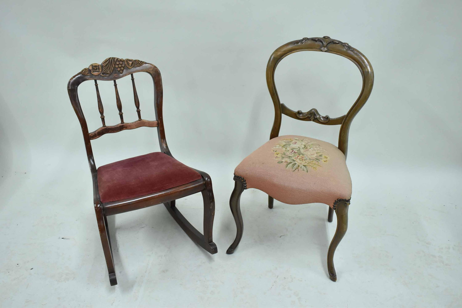 Victorian Wooden Carved Rocking Chair: Victorian Wooden Carved Rocking Chair with crushed velvet upholstery. Together with a needlepoint seated balloon back side chair. Used condition, surface distress. 30” x 18” x 18”