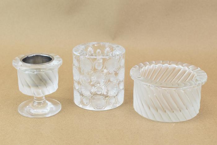 Three Assorted Vintage Lalique Glass Articles: Three Assorted Vintage Lalique Glass Table Articles comprising of a Tokyo pattern cigarette urn, a Smyrne pattern ashtray, and a Smyrne pattern candle holder, each signed at bottom Used condition, wea