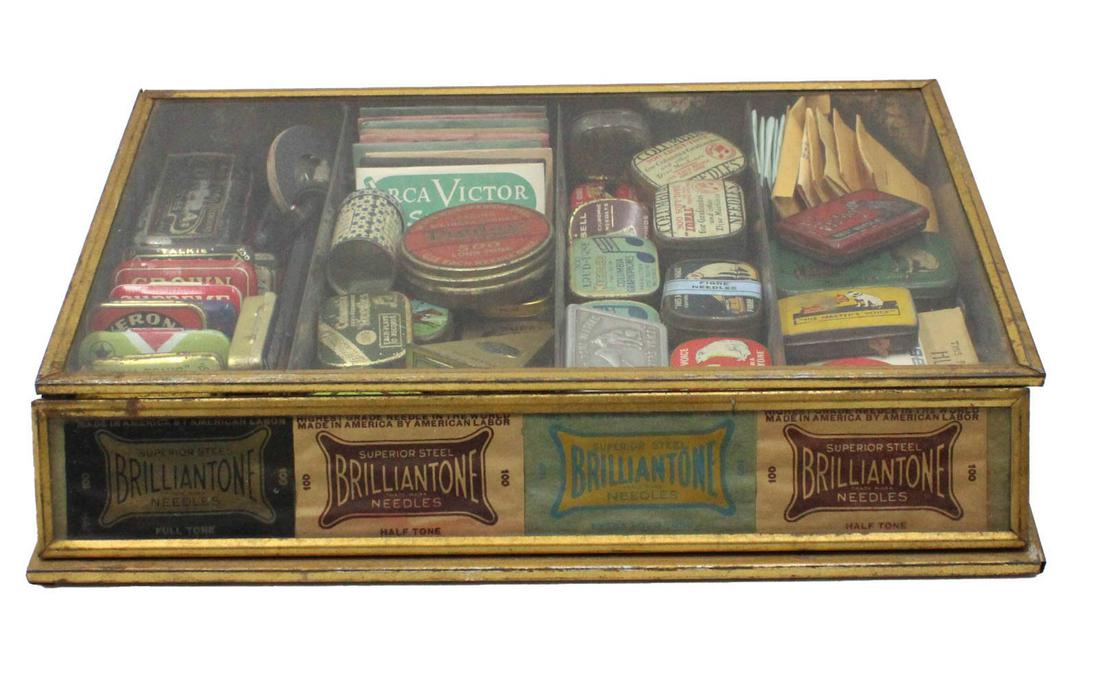 Group of Phonograph Needle Tins: Including tins from companies such as Victor and Columbia, in a presentational glass case