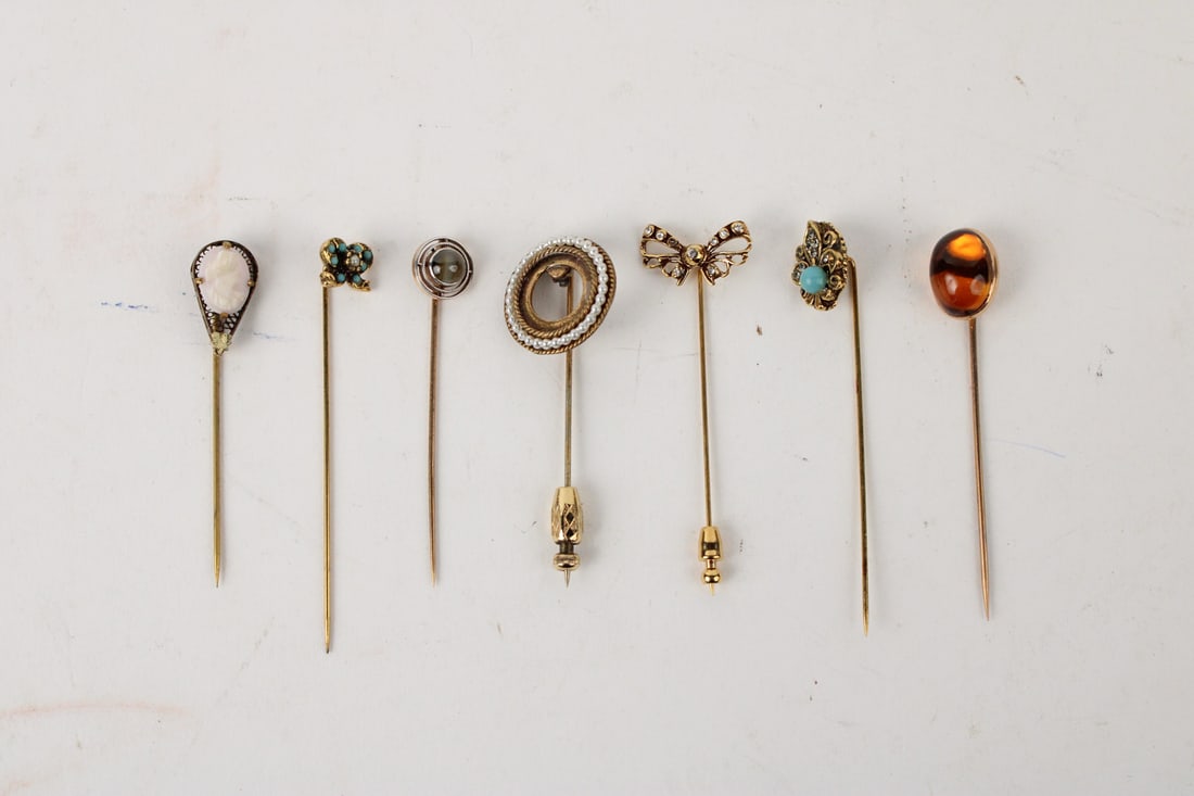 Group of Seven Gold Stick Pins: Group of Seven Gold Stick Pins, including one with seed pearls on circular top, bow, butterfly with turquoise beads, flour-de-lys with center turquoise, cat's eye, all approx. 3"l, used.