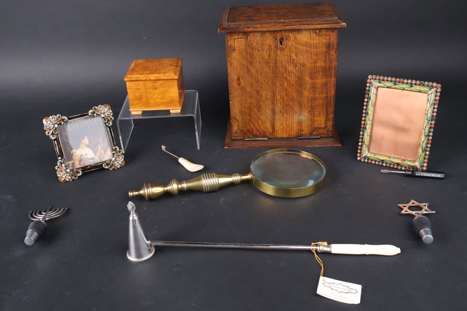 Group of Assorted Desk Articles: Group of Assorted Desk ArticlesComprising, an oak letter holder, a small box, a candlesnuffer, a magnifying glass, two wine stoppers, and two picture frames. 8 piecesProvenance: Property from the NAMI