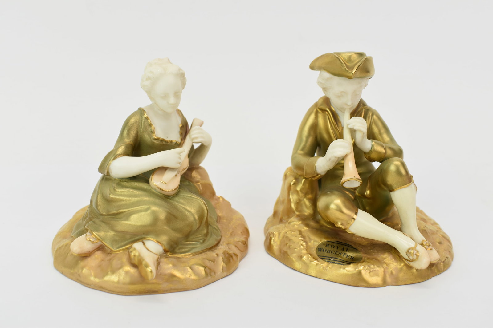 Jean Antoine Watteau Royal Worcester Pair of Musician Figurines: Jean Antoine Watteau Royal Worcester Pair of Musician Figurines Jean Antoine Watteau Royal Worcester Pair of Seated Musician Figurines featuring one of a man playing a pipe and a woman playing a small