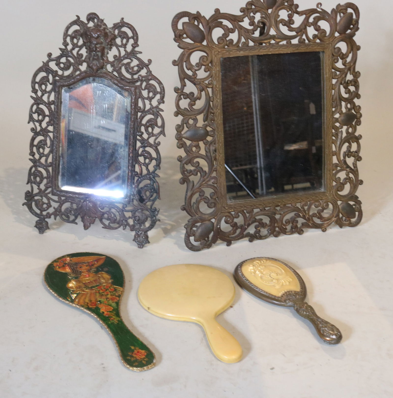 Two Bronze Table Mirrors along with Three Handheld Makeup Mirrors: Two Bronze Table Mirrors along with Three Handheld Makeup MirrorsComprising: One tabletop bronze framed mirror with foliate design; One wall-mounted bronze frame mirror; One bronze-based brass-stem ad