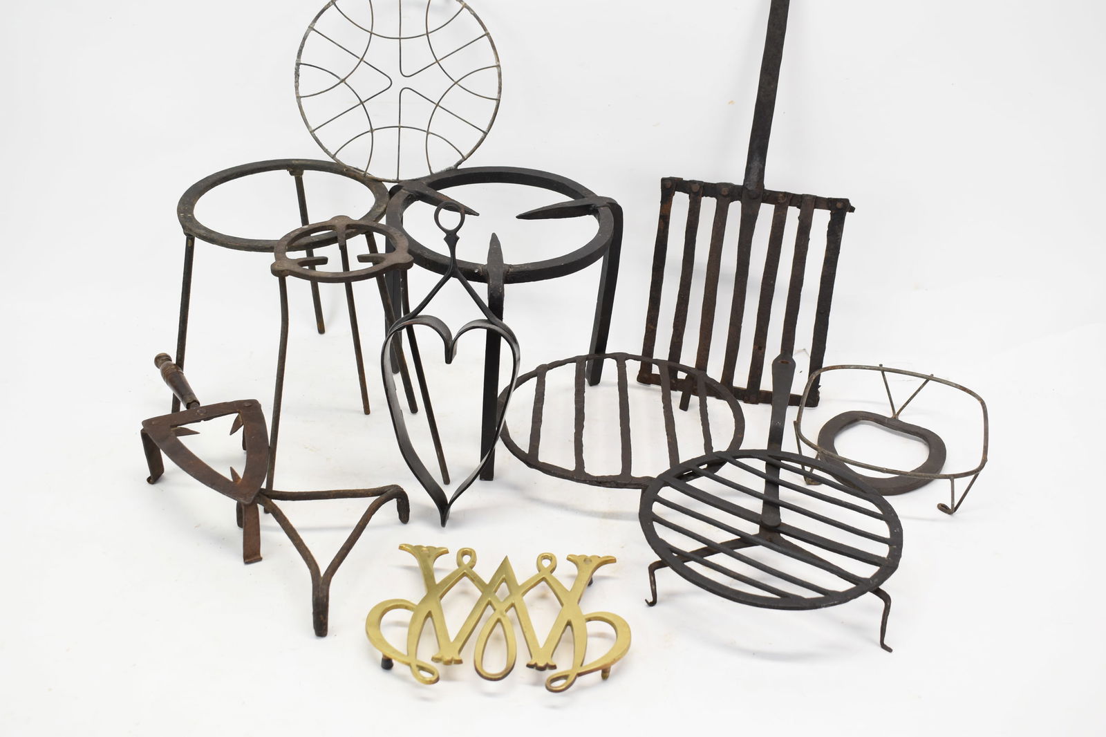 Group of Assorted Wrought Iron Fire Trivets: Group of Assorted Wrought Iron Fire TrivetsGroup of Assorted Wrought Iron Fire Trivets. Together with a marked William and Mary style brass trivet and a heart-form iron trivet.Used condition, wear, wo