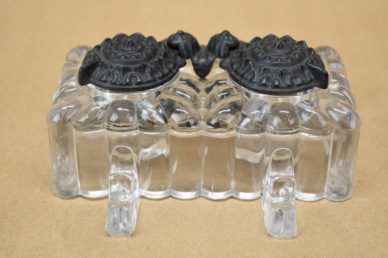 Glass and Cast-Iron Double Inkwell: Glass and Cast-Iron Double Inkwell Glass and Cast-Iron Double Inkwell, early 20th C. molded ribbed glass base with ornate pivoting lid covers. Used condition, wear, worn. 2 3/4"h x 6"w x 4 1/4"d
