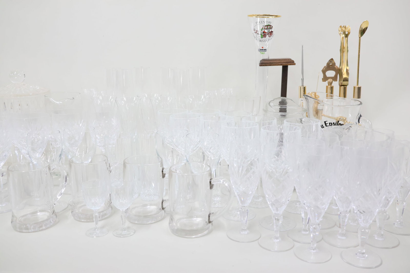 Large Group of Assorted Colorless Glass Barware: Large Group of Assorted Colorless Glass Barware Large Group of Assorted Colorless Glass Barware. Including large assortment of stemware, Orange peel texture pitcher, Fostoria coin pitcher, Heineken