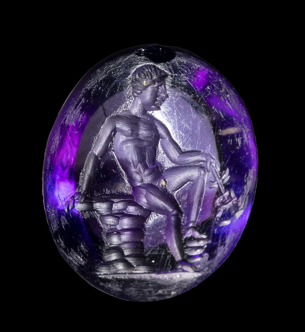 A FINE ROMAN AMETHYST INTAGLIO. SEATED HERMES WITH ATTRIBUTES.: A FINE ROMAN AMETHYST INTAGLIO. SEATED HERMES WITH ATTRIBUTES.1st - 2nd century A.D.10 x 12 x 3 mmThe young naked god is seated right on rocks, his left leg bent and his right foot on rocks, he holds