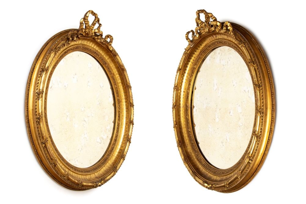 Pair of carved and gilded oval mirrors: Pair of carved and gilded oval mirrorsHeight x width x depth: 110 x 86 x 14 cmFrance, 19th centuryIn the Louis XVI style, the frames are topped by ornate cornices shaped like a knotted ribbon (a ̶