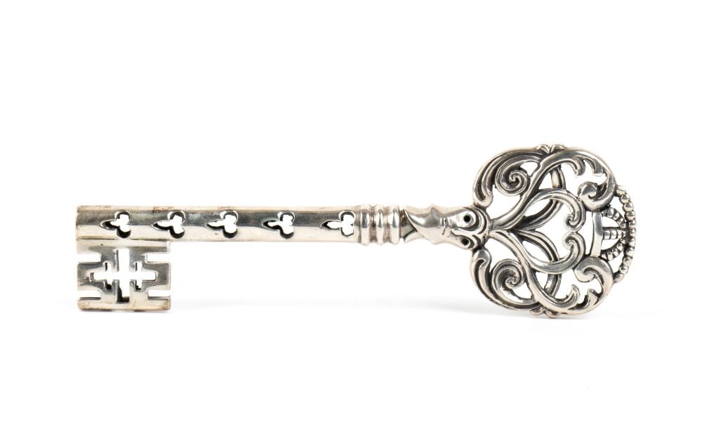 Collectors’ silver key: characterised by a finely openwork handle featuring Baroque motifs of volutes and curls, surmounted by a beaded crown. The shaft is entirely openworked with small trilobed, clover-shaped cut-outs, whi