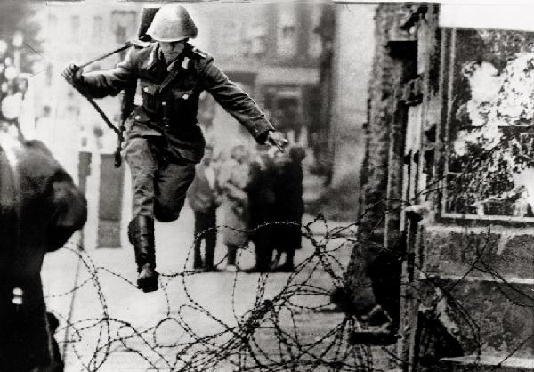 Leibing, Peter: East German soldier jumping over: East German border guard Konrad Schumann jumping over barbed wire line to West Berlin. August 15, 1961. Vintage ferrotyped gelatin silver print (wire photo). 17 x 23,7 cm. Various agency stamps, annot