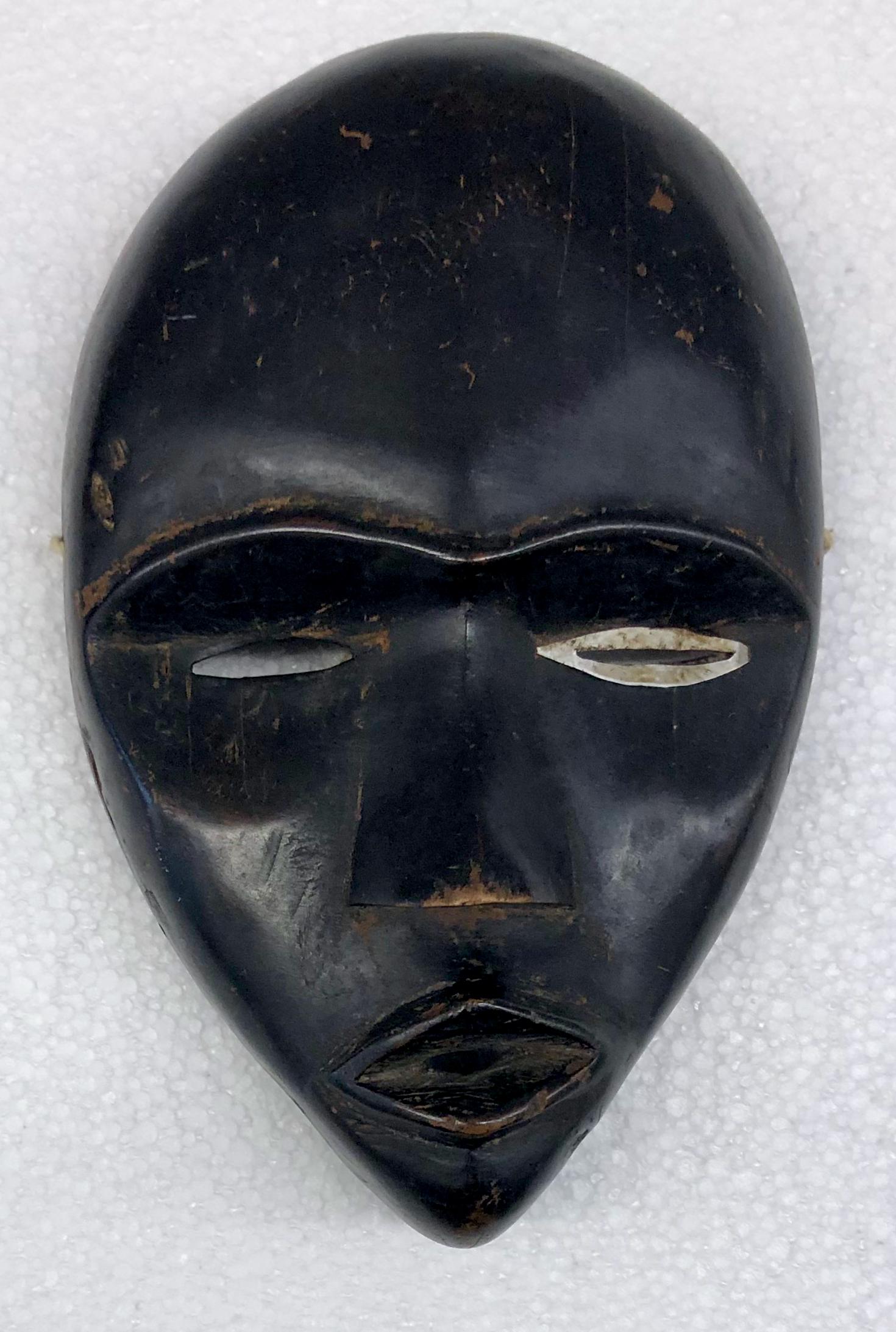 Antique Carved Dan Mask: Early hand-carved Dan African mask, Ivory Coast. Hand carved wood, slit eyes with metal insert and diamond shaped mouth. Circa 1920s. Dimension: H: 11 in. x W: 6.75 in x D: 2.6 in. Condition: no repai