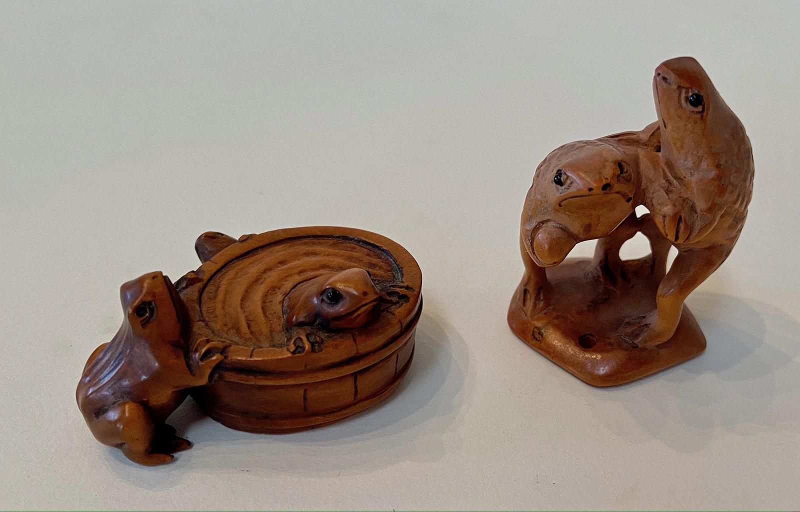 Japanese Carved Wood Netsuke Frogs & Toads: Two Japanese Carved Wood Netsuke with inlaid eyes. Three toads around a water bucket, artist signed (view photo). Dimension: height: 1 3/4 in. Two standing frogs. Dimension: height: 2 1/8 in. Conditio