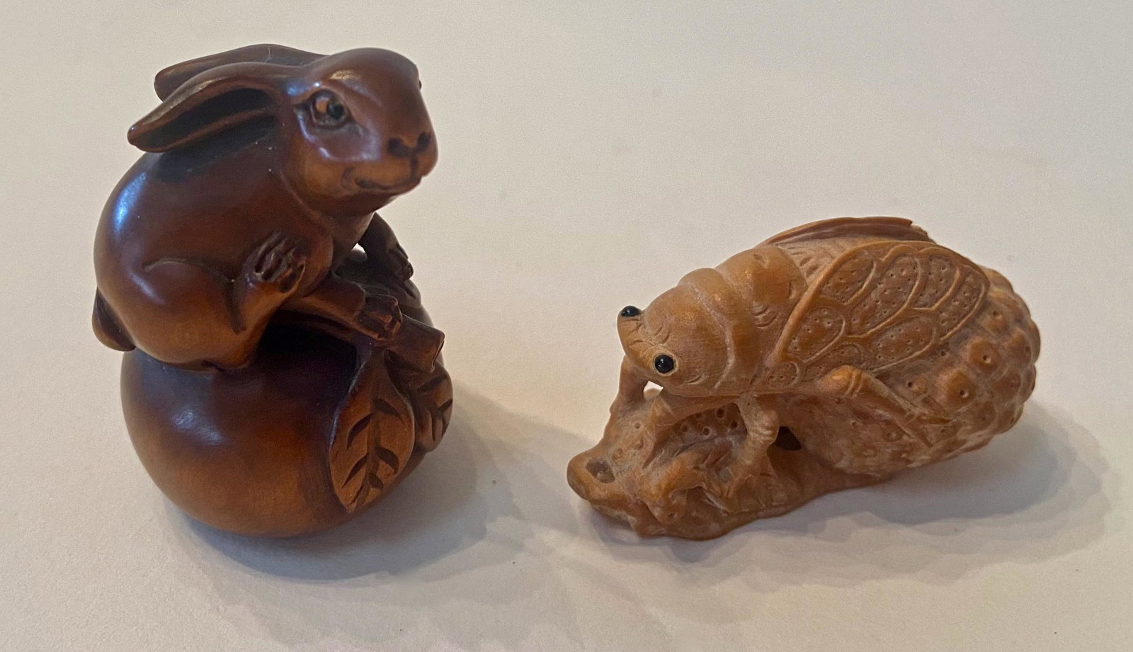 Japanese Carved Wood Netsuke, Form Of Cicada And Rabbit: Two Japanese Carved Wood Netsuke. Carved Rabbit atop Acorn, artist signed. Dimension: height: 1 in. Carved Cicada perched on leaf. Dimension: height: 1 3/4 in. Condition: both carvings are in good ori
