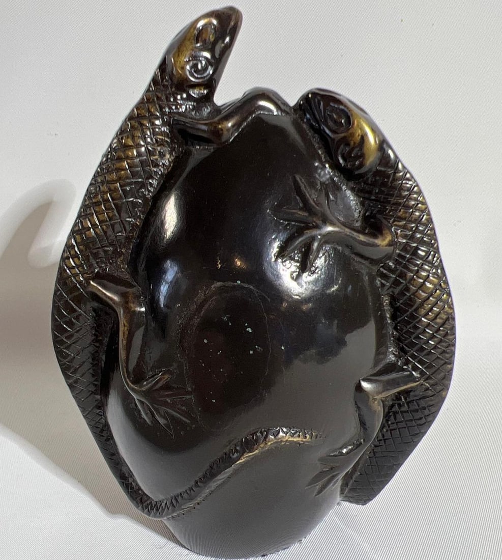 BRASS LIZARDS ON AN EGG PAPERWEIGHT: This intriguing brass sculpture or paperweight depicts two lizards entwined around an egg, creating a visually dynamic and symbolic piece. The use of brass gives the object a warm, metallic sheen and