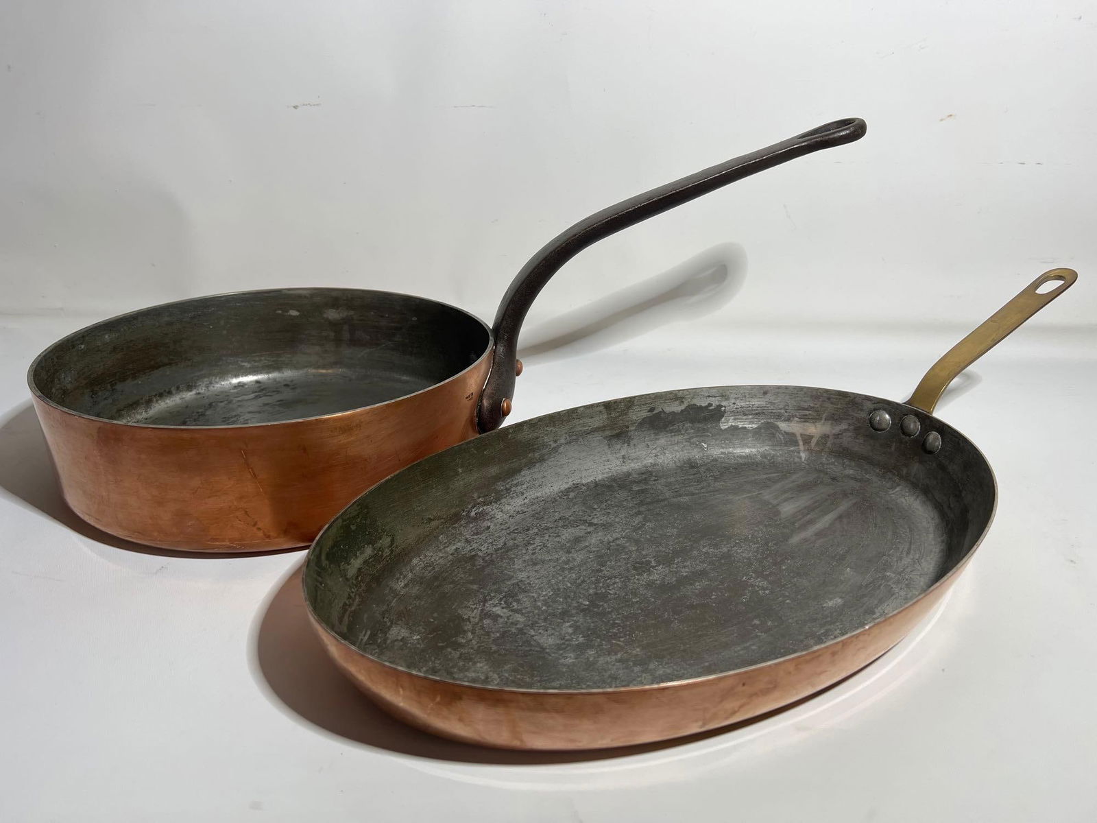 LIVING ESTATE OF JOSEPH RODANO: PAIR OF HEAVY COPPER PANS | MADE IN FRANCE: This pair of heavy copper pans, made in France, represents high-quality cookware prized for its excellent heat conductivity and even heating. The set includes two distinct pan types: one with a straig