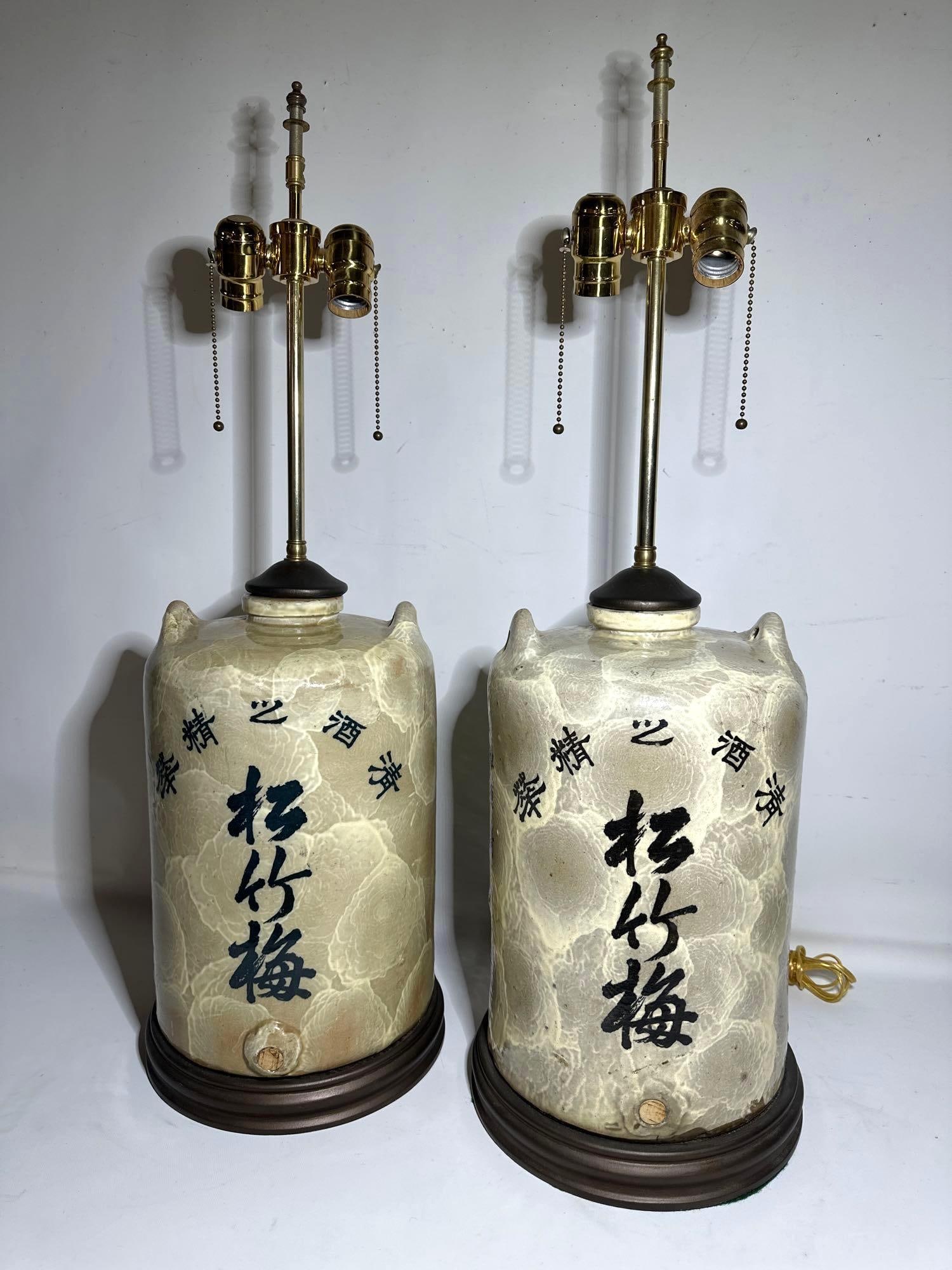 PAIR OF VINTAGE JAPANESE SAKE JAR LAMPS: This distinctive pair of vintage Japanese sake jar lamps offers a unique blend of traditional Japanese aesthetic repurposed for a modern use. The lamps are crafted from repurposed sake jars, ceramic v