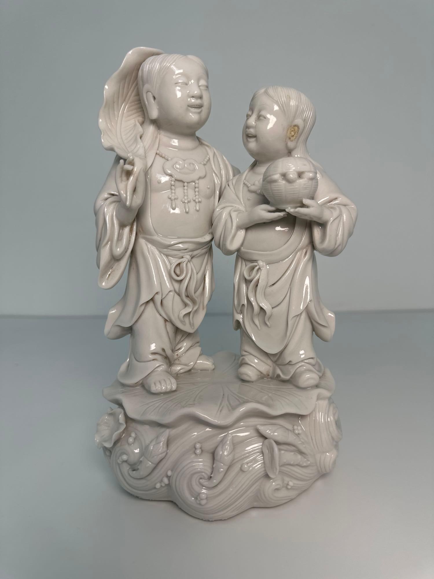 CHINESE BLANC DE CHINE HEHE TWINS LATE 19TH - EARLY 20TH CENTURY: This charming Chinese Blanc de Chine Hehe Twins sculpture, fresh from the estate of a lifelong collector of Asian art, captures the essence of childhood innocence and joyful companionship. Crafted in 