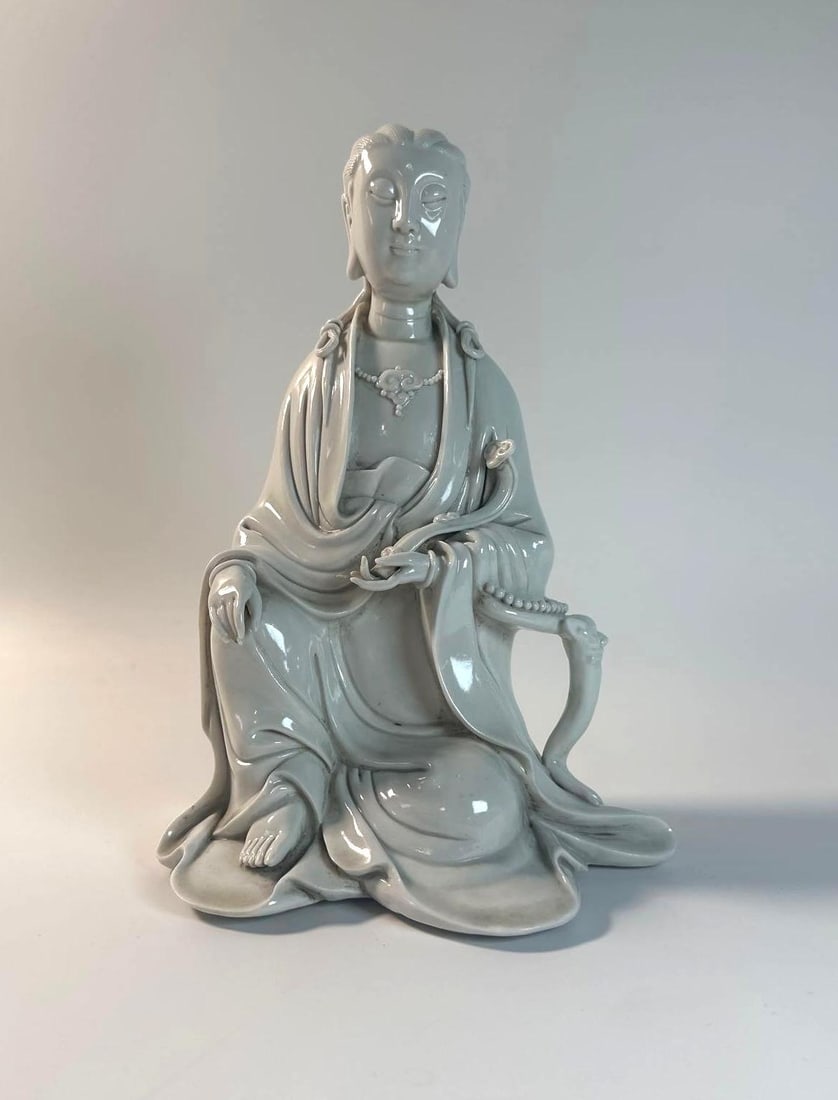 CHINESE BLANC DE CHINE DEHUA PORCELAIN SEATED GUANYIN STATUE: This elegant Chinese Blanc de Chine Dehua porcelain statue, standing 10 inches tall, depicts a seated Guanyin, the bodhisattva of compassion, showcasing the serene beauty of Buddhist art and the refin