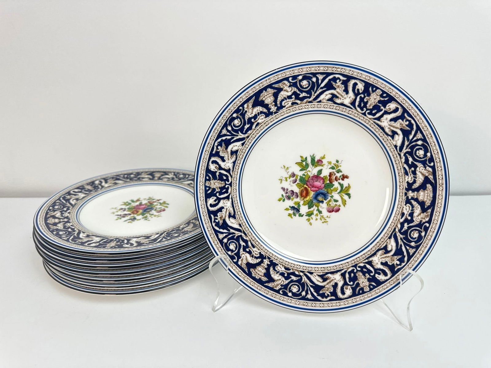 VALUE LOT! WEDGWOOD FLORENTINE 8 PIECE SET DARK COBALT BLUE APPETIZER PLATES: An eight-piece set of Wedgwood Florentine appetizer plates, each featuring a white center decorated with a colorful floral bouquet, surrounded by a wide, dark cobalt blue rim with an ornate, repeating