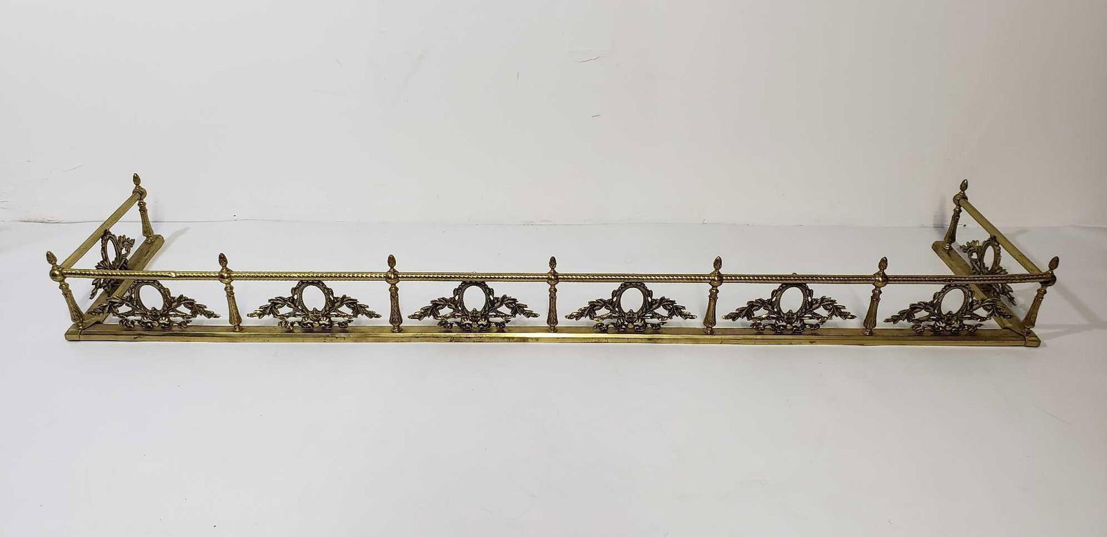 VALUE LOT BRASS LAUREL WREATH AND LEAF MOTIF FIRE FENDER: This brass laurel wreath and leaf motif fire fender, measuring 7.75" x 76.5" x 17.5", exemplifies the elegance of Neoclassical design, reminiscent of the Empire and Gilded Age periods, making it a stu